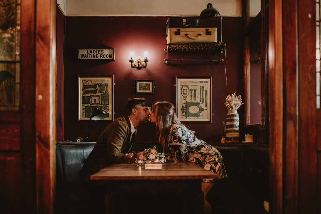 Bride and groom kiss across a wooden pub table during their intimate Sheffield wedding, captured by a natural and emotive Sheffield wedding photographer.